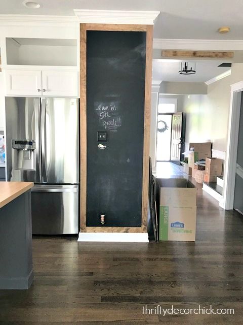 an empty kitchen with a chalkboard on the wall and refrigerator in the back ground