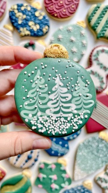 a hand holding a decorated christmas ornament in front of cookies on a table