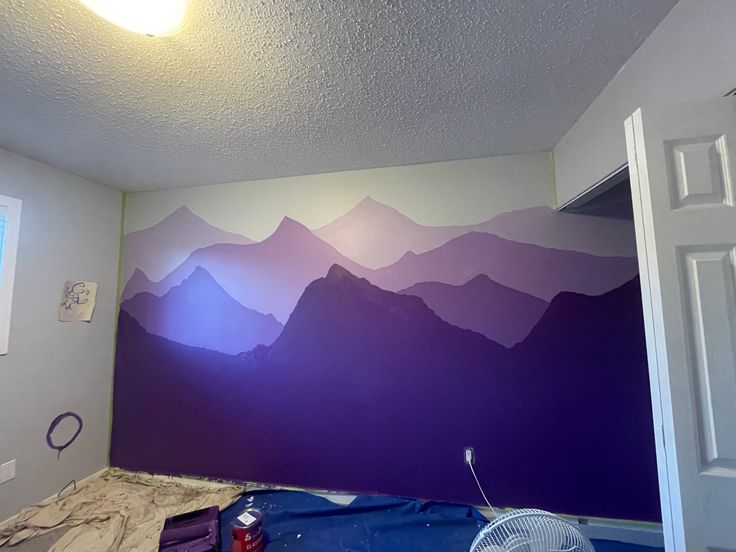 a room with mountains painted on the wall and a fan in it's corner