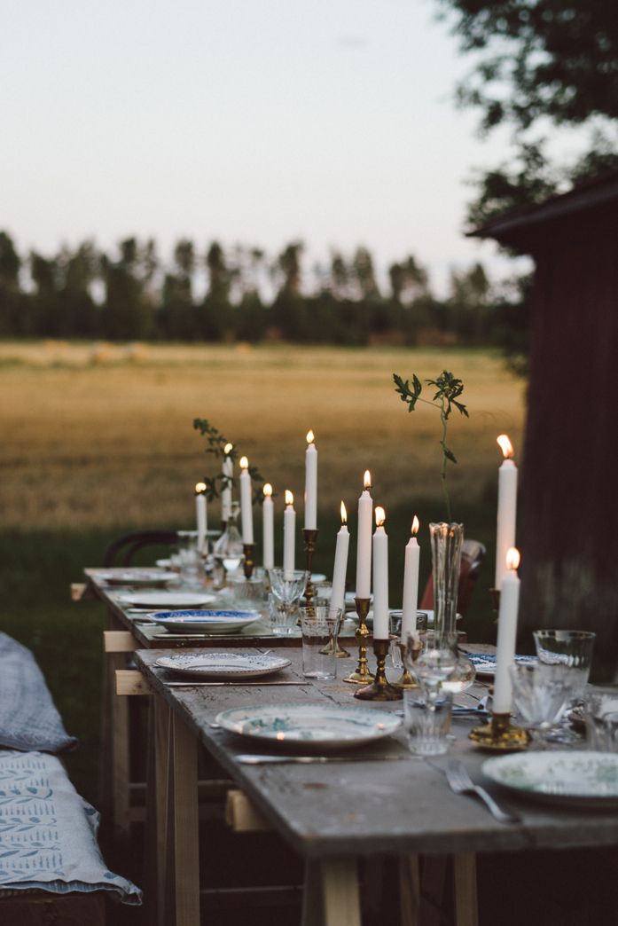 a long table is set with candles and place settings for an outdoor dinner party in the evening