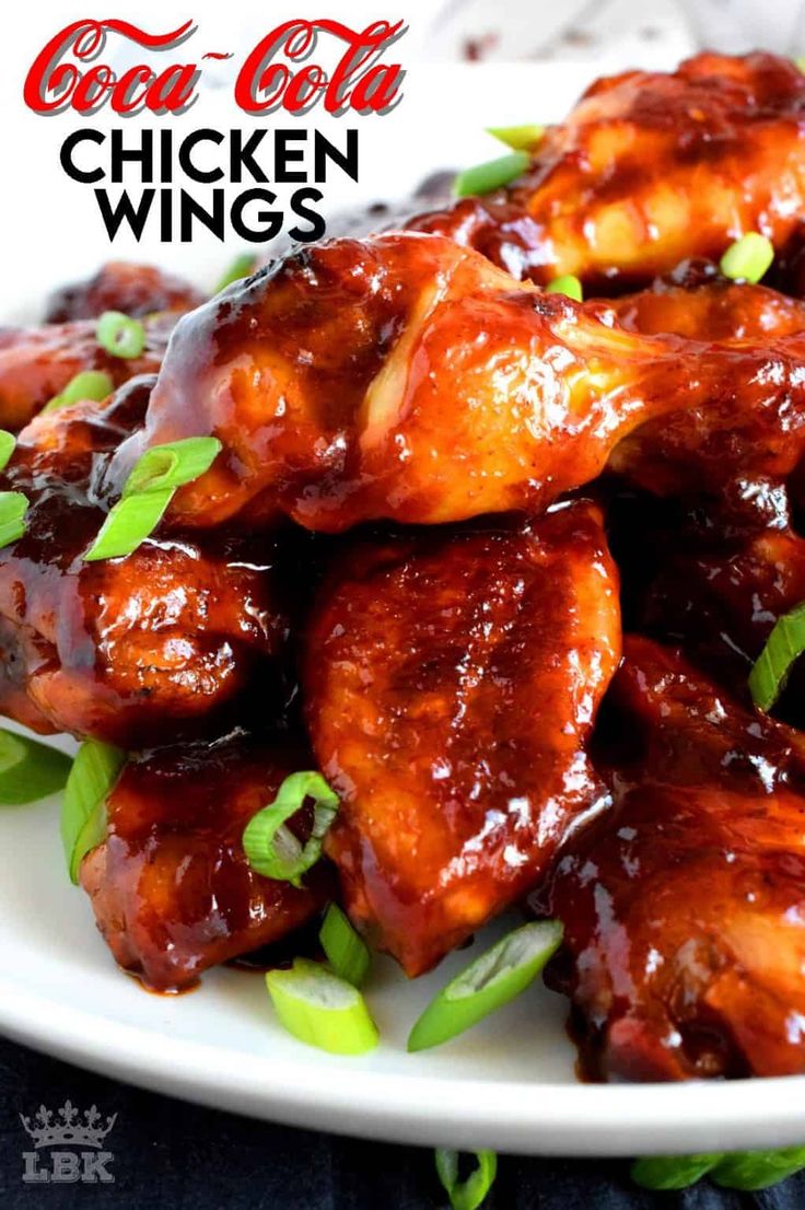 a white plate topped with chicken wings covered in bbq sauce and garnished with green onions