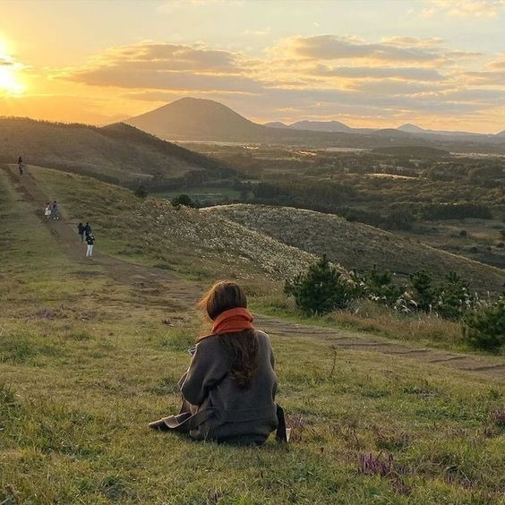 a woman sitting on top of a lush green hillside