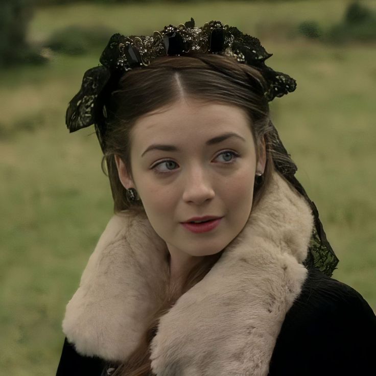 a woman wearing a fur collar and black dress in a field with grass behind her