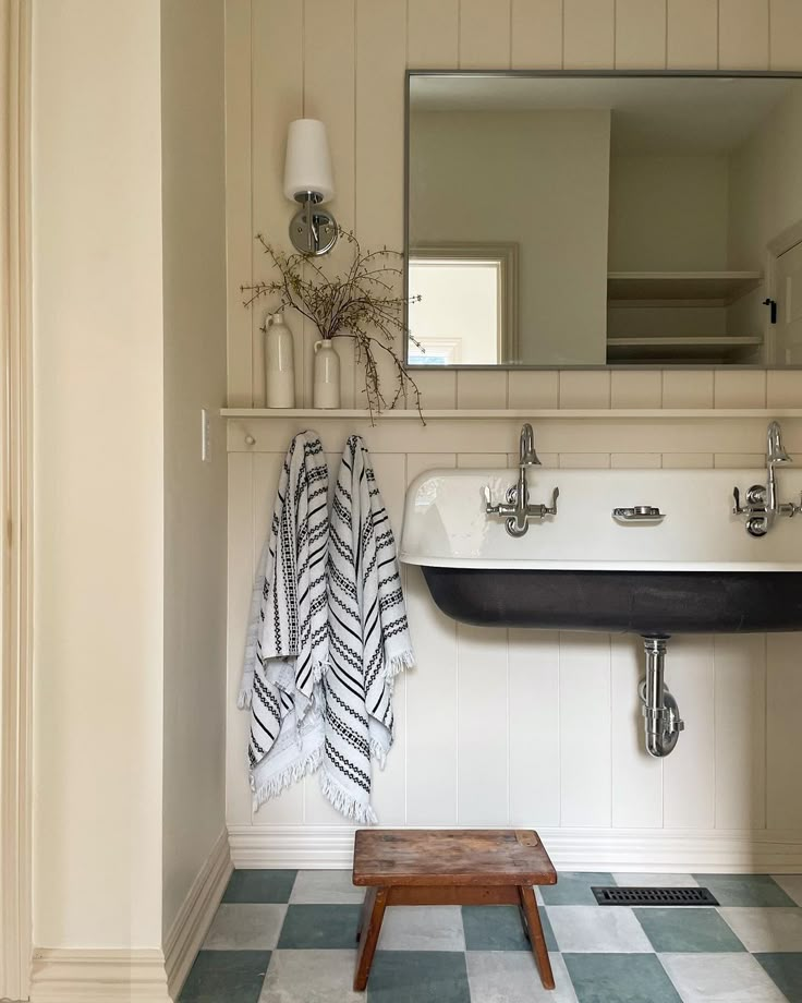 a bathroom with checkered flooring and white walls, black sink and mirror on the wall