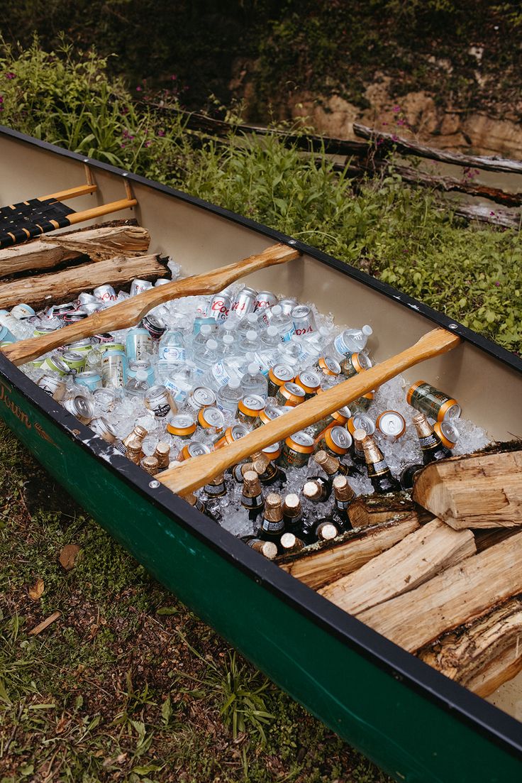 an empty canoe filled with bottles and wooden sticks sitting on the ground next to grass