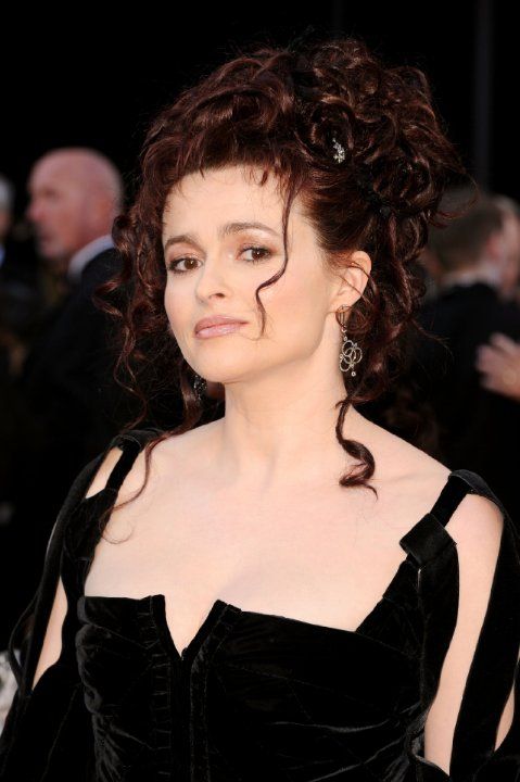 a woman with curly hair wearing a black dress and diamond earrings on the red carpet