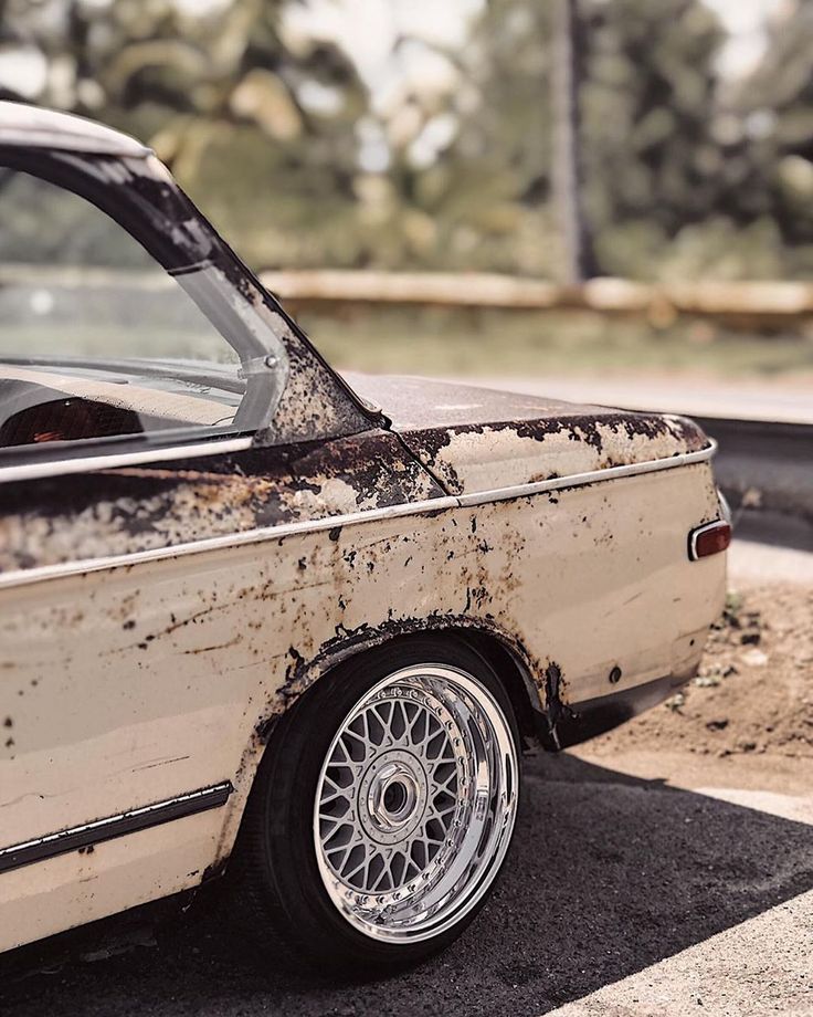 an old, dirty car is parked on the side of the road