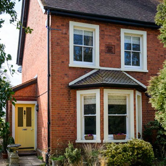 a red brick house with white windows and yellow door in the middle of a garden