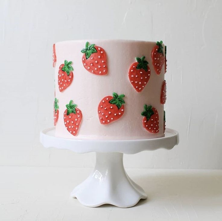 a pink cake with strawberries on it sitting on a white pedestal next to a wall