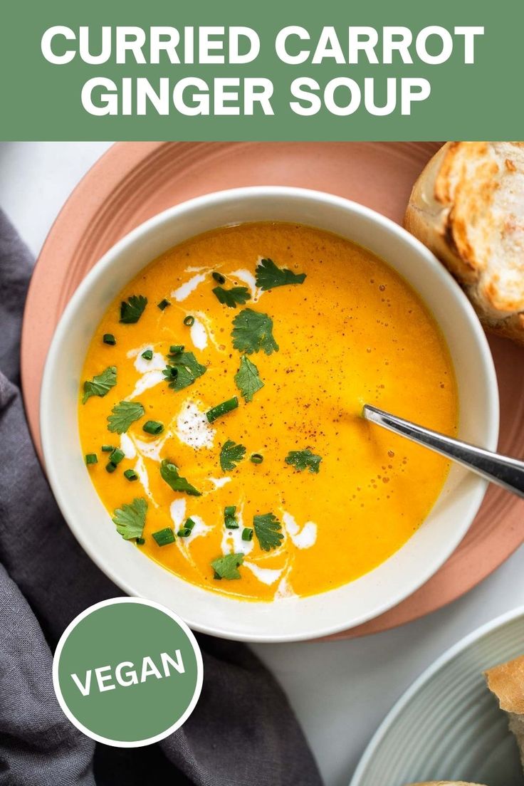 a bowl of carrot ginger soup on a plate with bread and garnishes