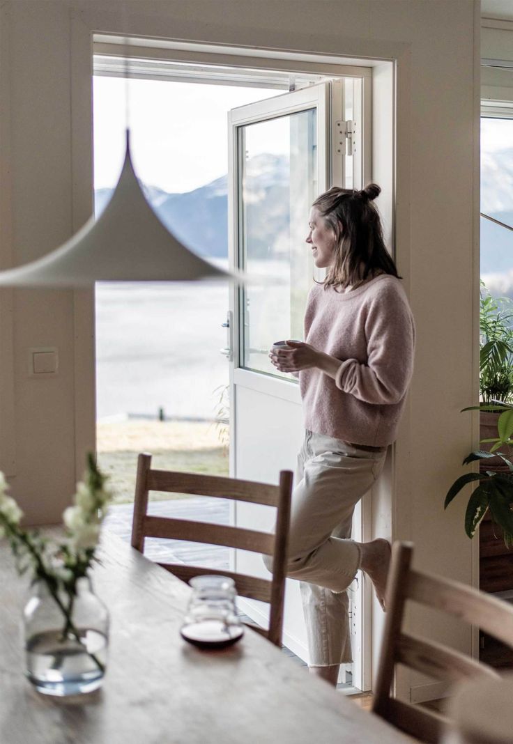 a woman standing in front of a window next to a table