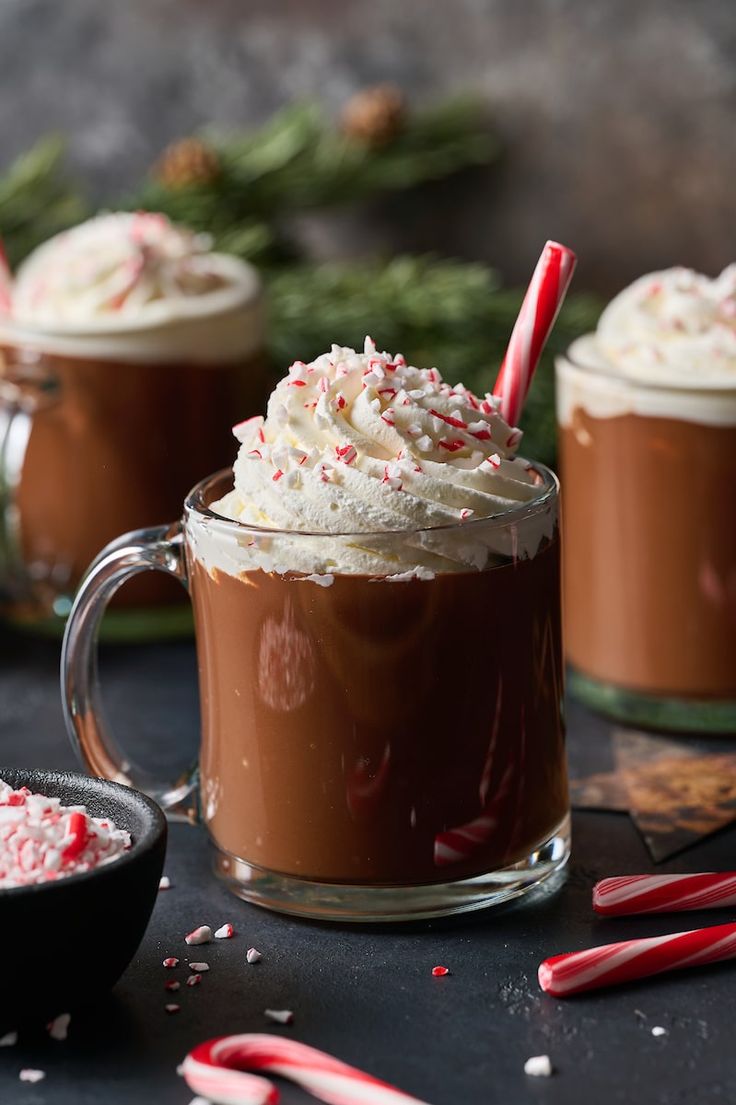 two mugs filled with hot chocolate and candy canes on top of a table