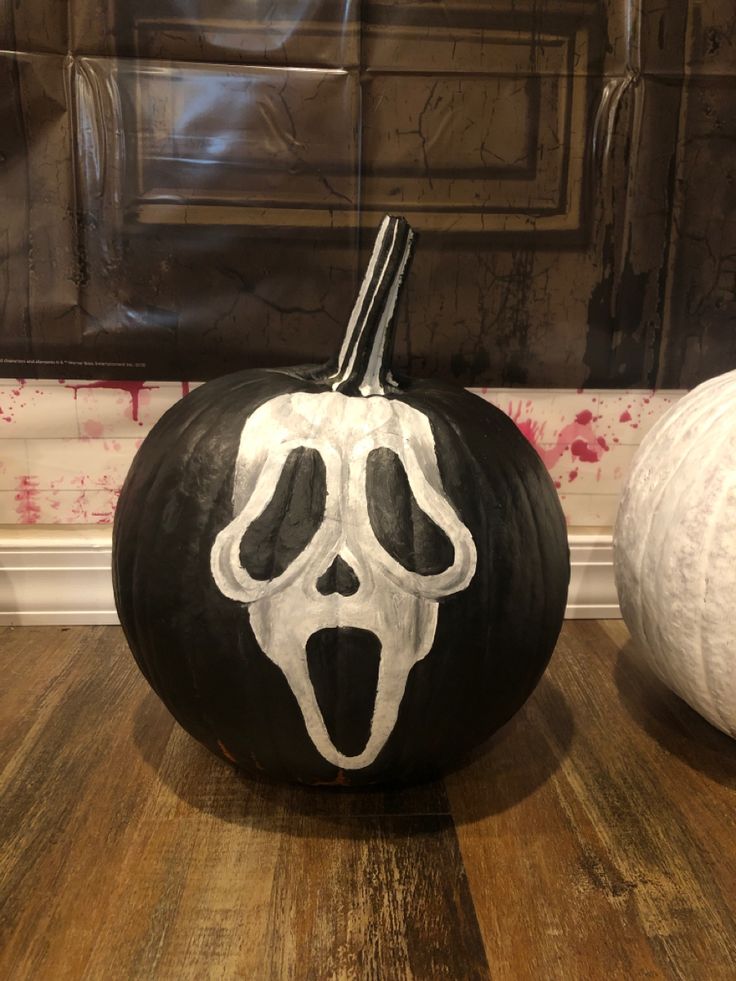 a black and white pumpkin with a skeleton face painted on it sitting in front of a wall