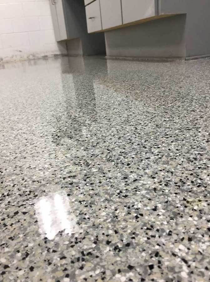 a kitchen floor with black and white speckles on the top, and cabinets in the background