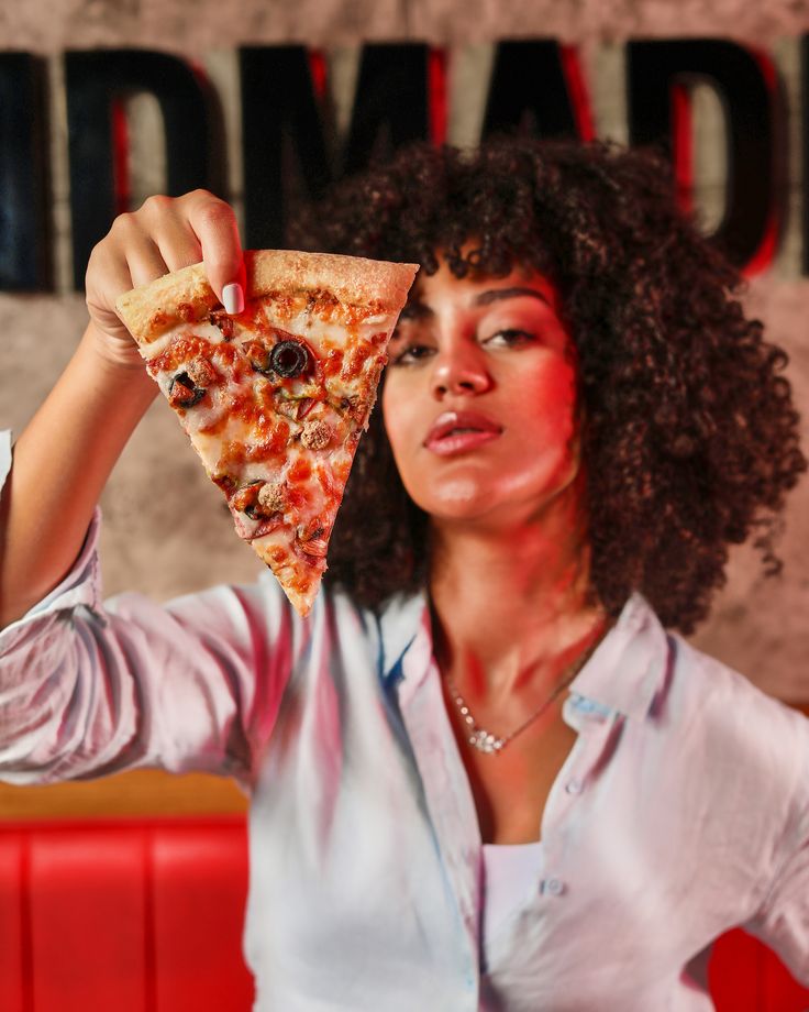 a woman holding up a slice of pizza in front of her face