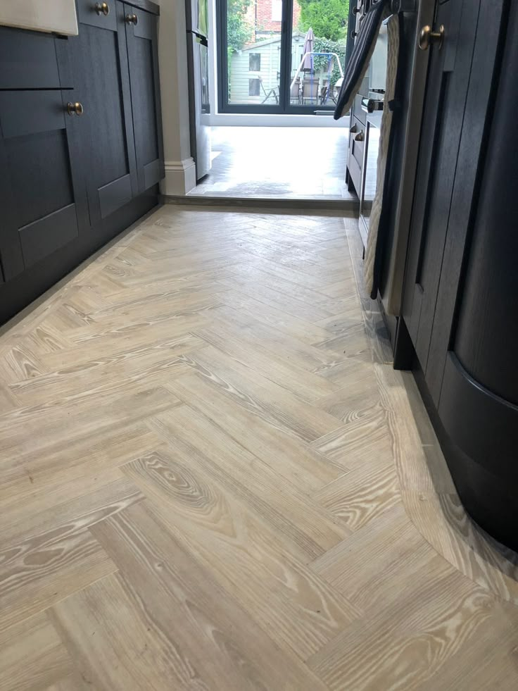 a kitchen with wood flooring and black cabinets in the backround, next to a large window