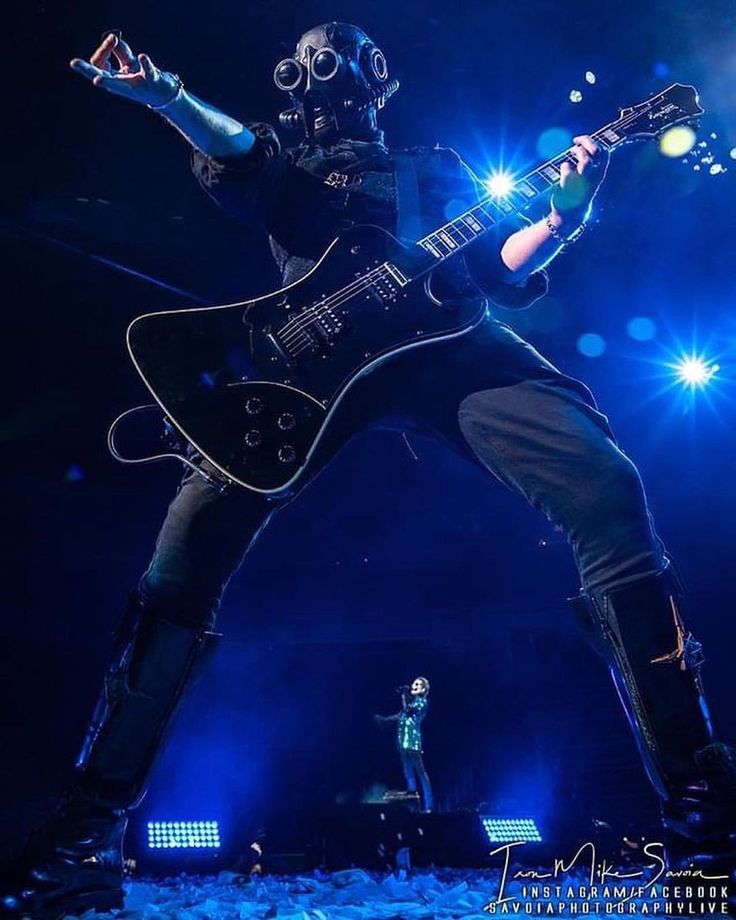 a man with a guitar in his hand and some blue lights behind him on stage