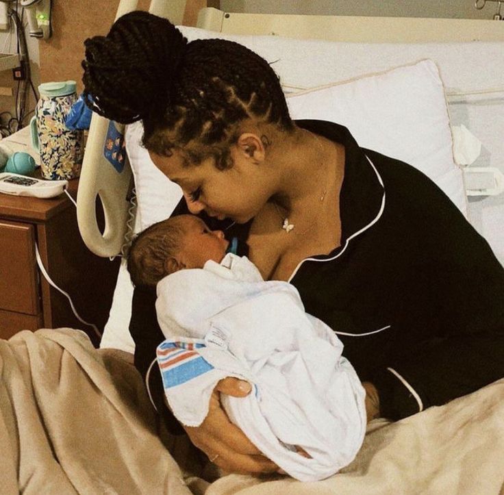 a woman holding a baby in her arms on top of a bed next to a night stand