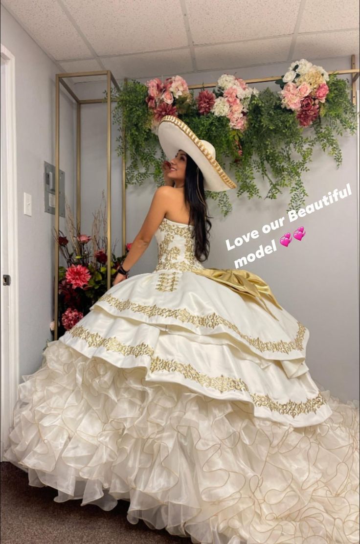 a woman in a white dress and hat with flowers on the wall next to her