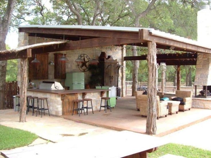 an outdoor kitchen with bars and stools on the outside patio, surrounded by trees