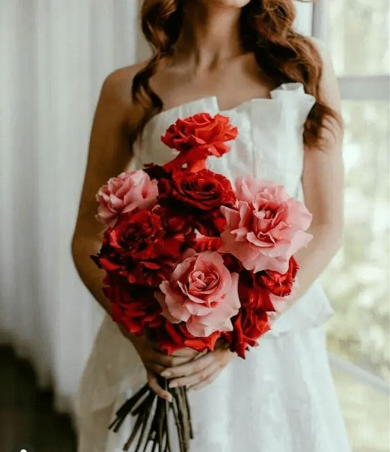 a woman holding a bouquet of red and pink flowers