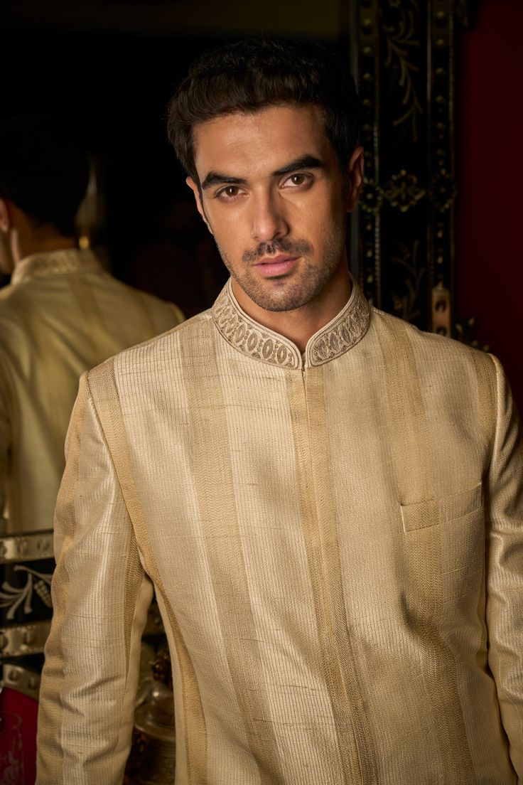 This set features stitch lines in gold thread in a stripe pattern. The collar has delicate dori embroidery. It is paired with a matching cotton silk kurta and straight pants. Complimenting stole and footwear is also available. DELIVERY TIMEPlease allow 8-12 weeks for your outfit to arrive. FABRIC DETAILSSherwani - Raw Silk, Kurta - Cotton Silk, Trouser - Cotton Silk, Dupatta - Cotton Tissue Organza Professional cleaning only. Elegant Silk Sherwani With Traditional Drape, Elegant Raw Silk Sherwani With Traditional Drape, Elegant Silk Sherwani With Resham Embroidery, Elegant Gold Unstitched Suit For Transitional Season, Elegant Gold Unstitched Suit For Festive Occasions, Designer Gold Sets With Naqshi Detailing, Elegant Raw Silk Nehru Jacket With Naqshi, Elegant Sherwani In Raw Silk With Straight Kurta, Elegant Raw Silk Sherwani Straight Kurta