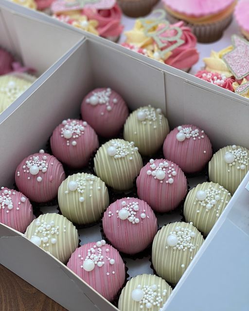 some pink and white cupcakes in a box on a table with other cupcakes