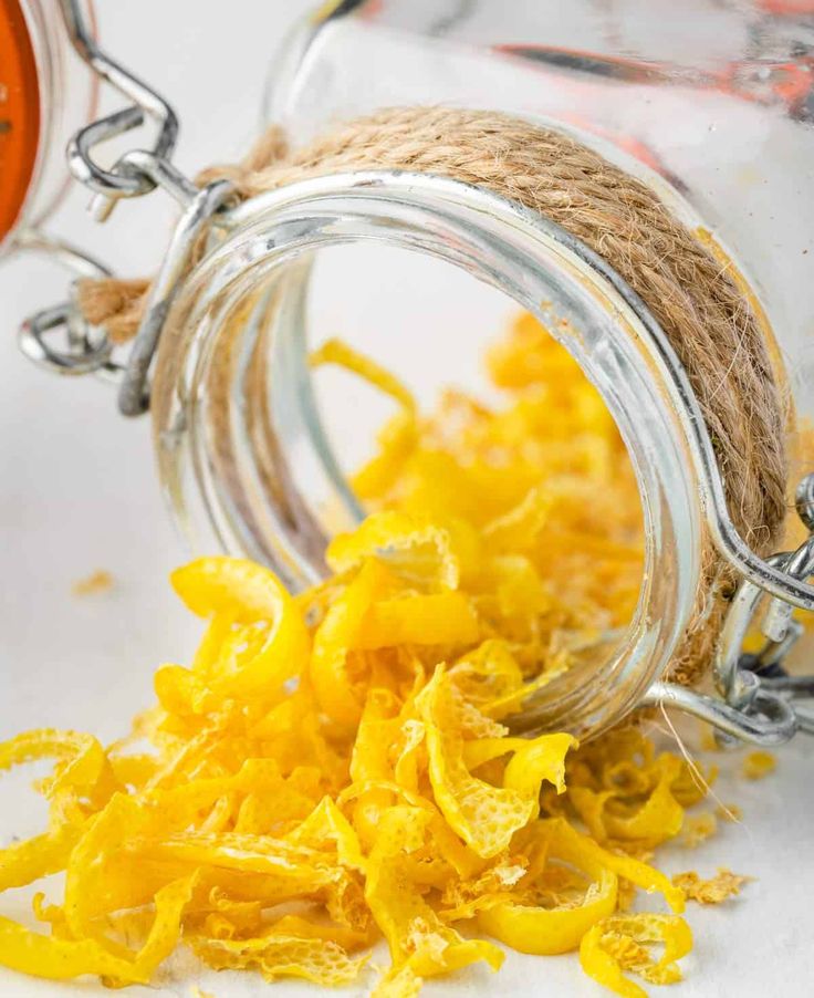 a jar filled with dried yellow flowers sitting on top of a white table next to a rope