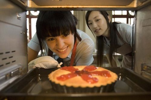 two women are looking at a cake in the oven with toppings on it and one is smiling