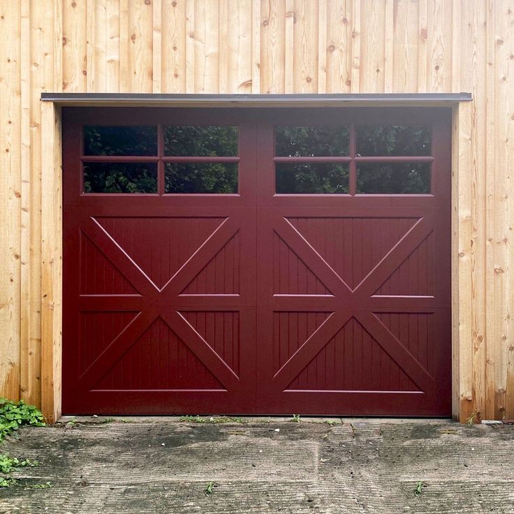 a red garage door is open in front of a wooden wall and green grass on the ground