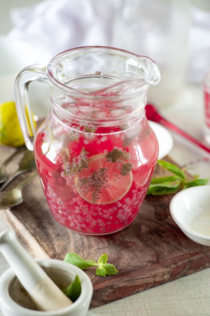 rose basil lemonade in a glass pitcher on a wooden cutting board with spoons