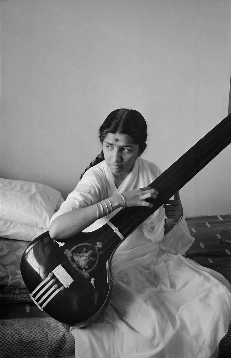 a woman sitting on top of a bed while holding an acoustic guitar in her hands