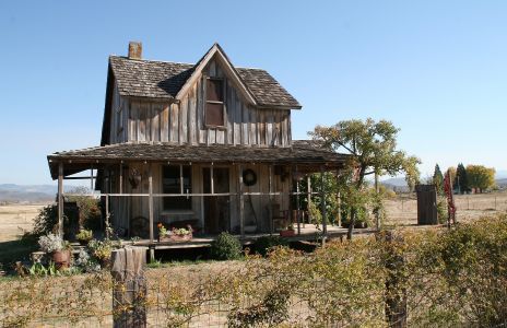 an old wooden house sitting in the middle of a field