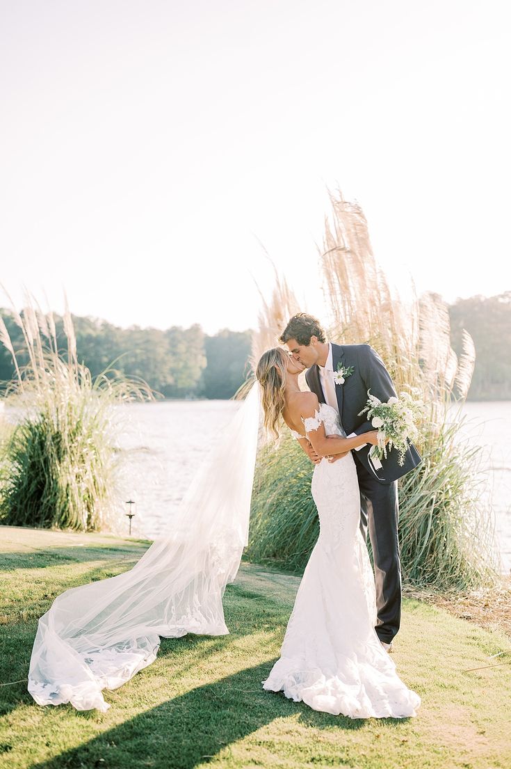 a bride and groom kissing in front of the water