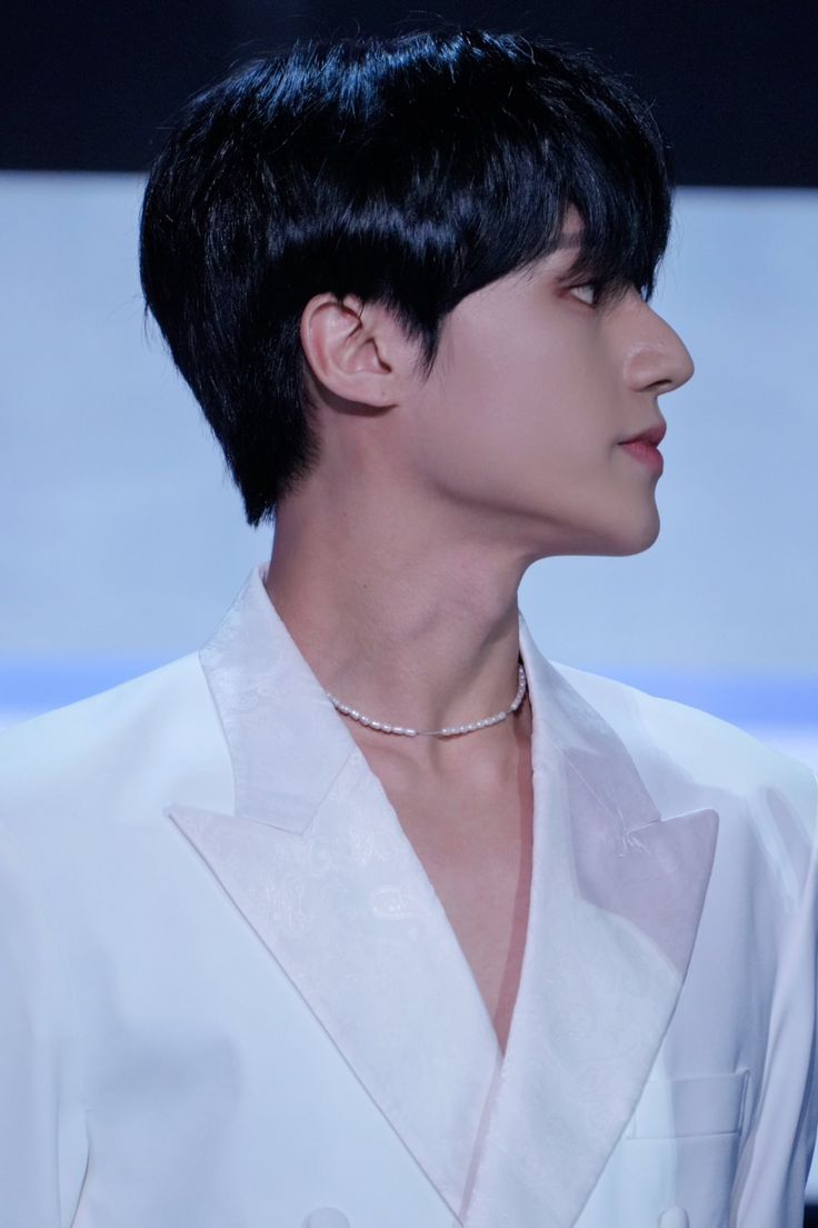 a man with black hair wearing a white suit and diamond choker on his neck