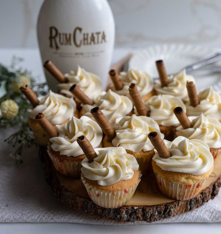 cupcakes with white frosting and cinnamon sticks are arranged on a wood slice