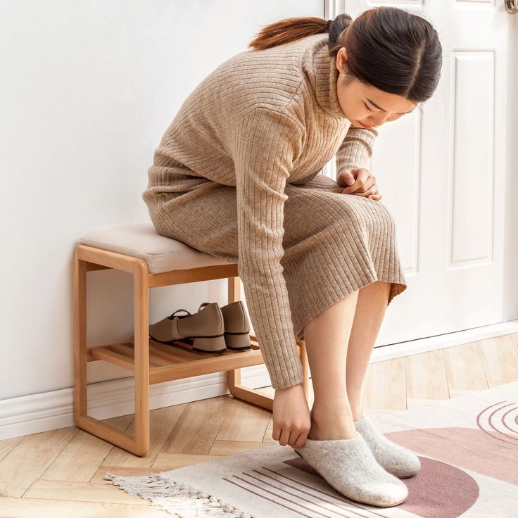 a woman is sitting on a stool and tying her shoes with one hand while looking down at the ground