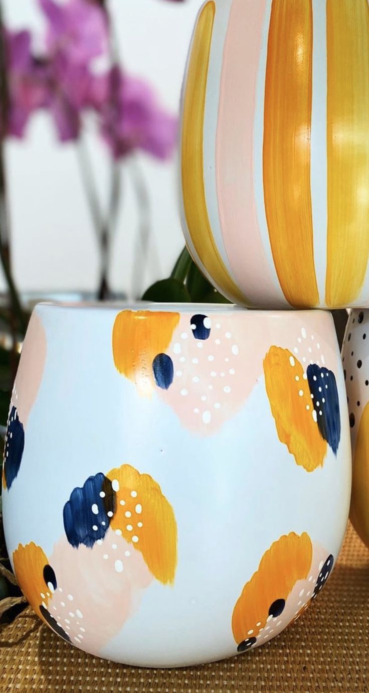 two colorful vases sitting next to each other on top of a wooden table with flowers in the background