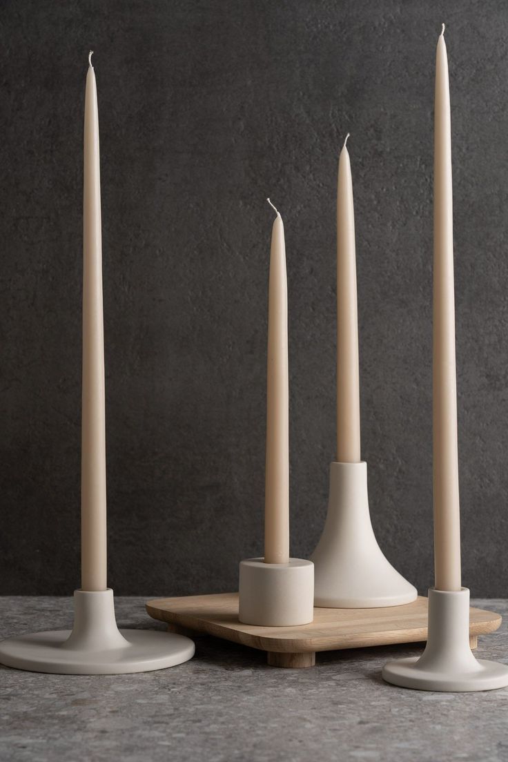 three white candles sitting next to each other on top of a wooden tray in front of a gray wall