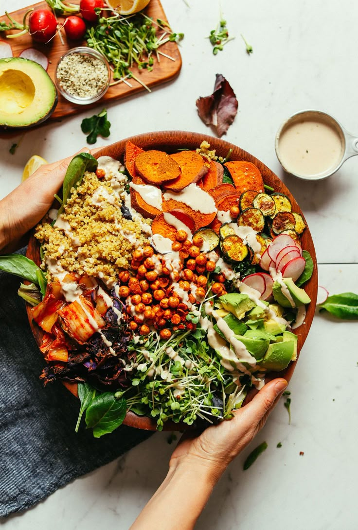 two hands holding a large bowl filled with different types of salads and dressings