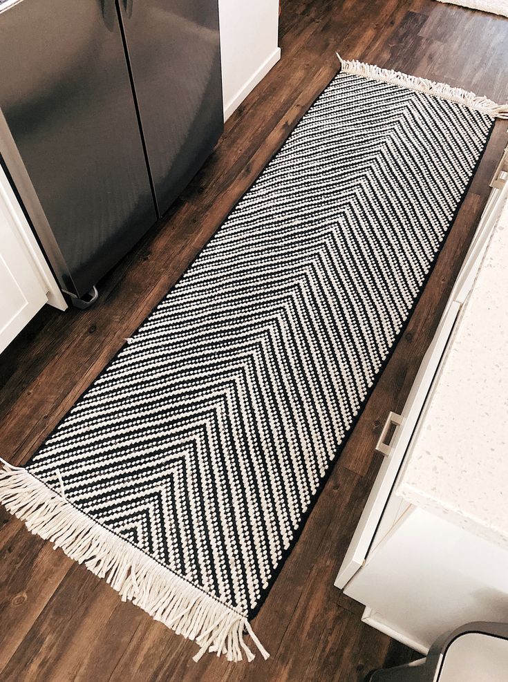 a black and white rug sitting on top of a wooden floor next to a refrigerator