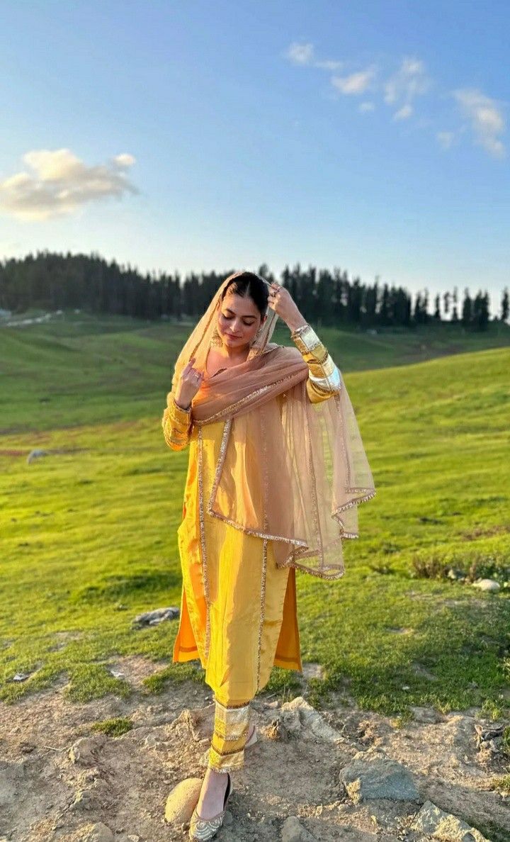 a woman standing on top of a lush green field wearing a yellow outfit and veil