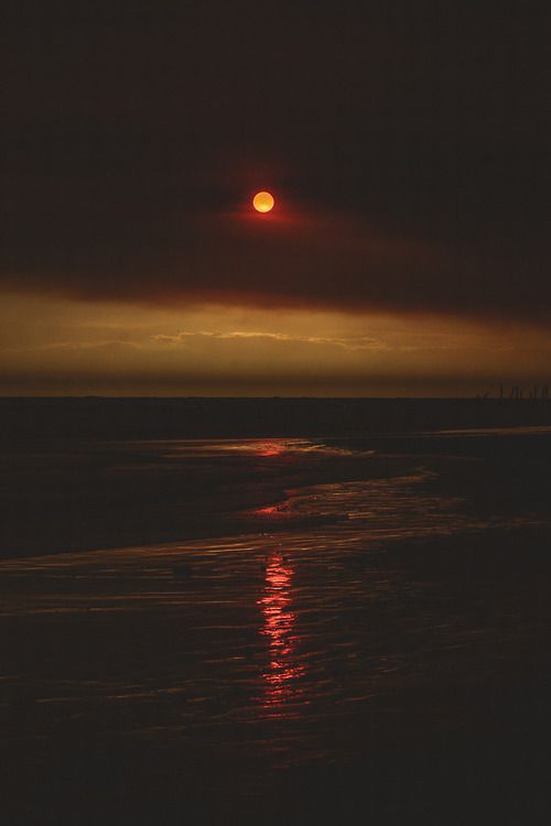 the sun is setting over the ocean with dark clouds and red light in the sky