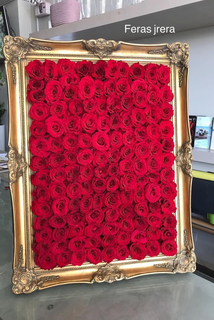 a gold frame filled with red roses on top of a glass table in a store