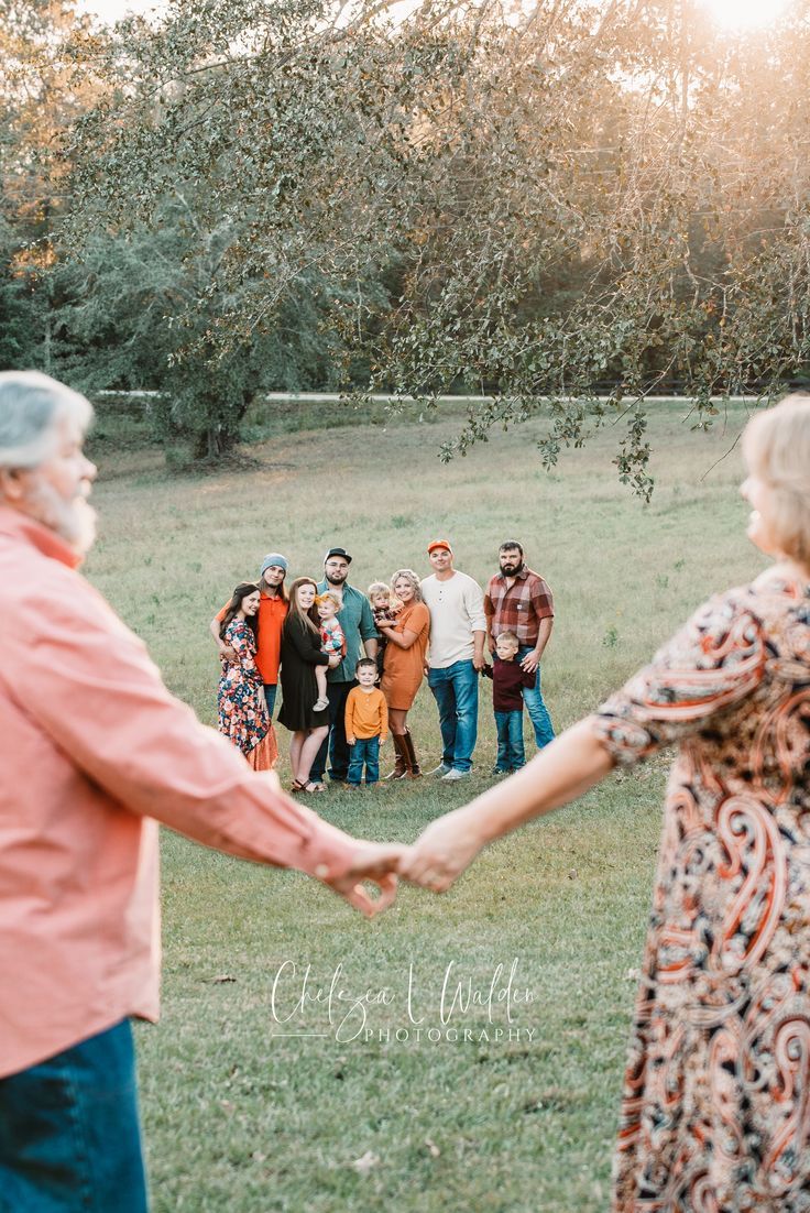 a group of people holding hands in the middle of a field with trees and grass