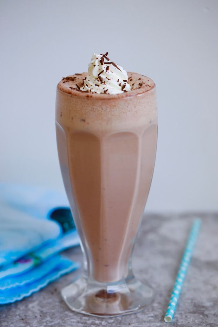 a chocolate drink with whipped cream in a tall glass next to a blue and white straw