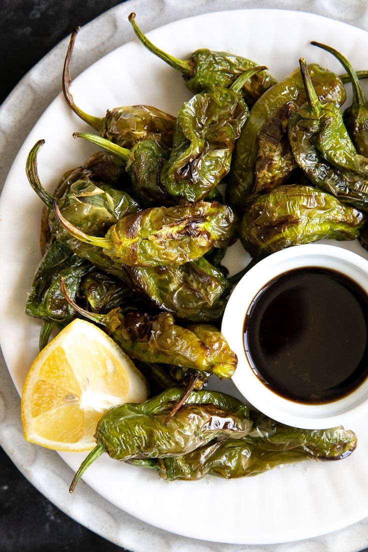 a white plate topped with green peppers next to a cup of black liquid and lemon wedges