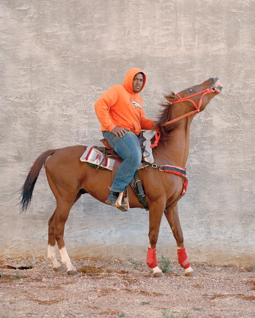 a man in an orange hoodie is riding a brown horse