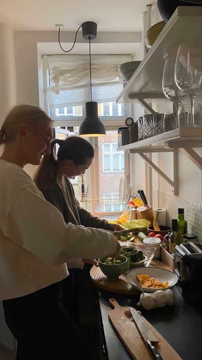 two women preparing food in a kitchen with open shelving and shelves on the wall