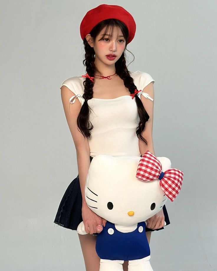 a girl in a dress and hat holding a hello kitty stuffed animal